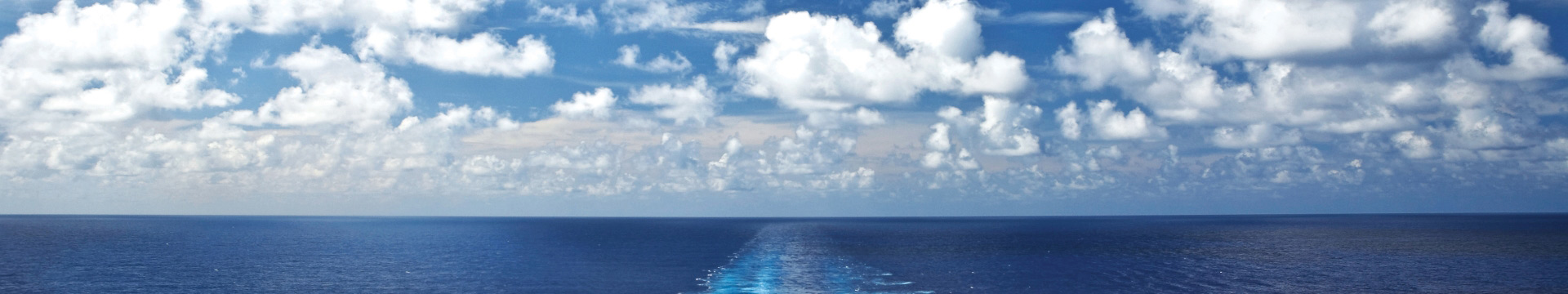 Ocean with ship trail with fluffy white clouds and a deep blue sky.
