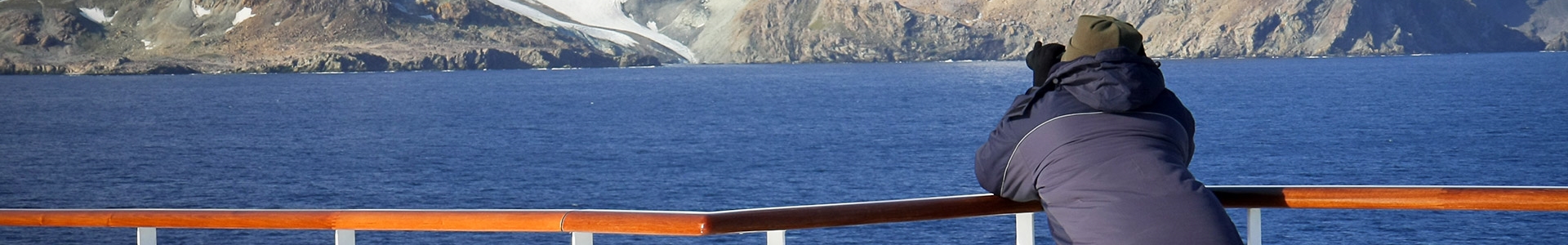 Person on a ferry taking photos of snowy mountains in the distance.